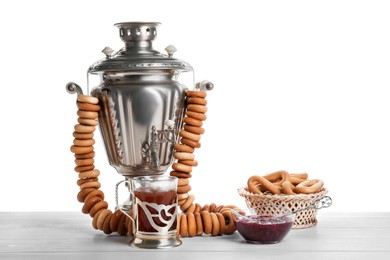 Photo of Samovar with hot tea, jam and delicious ring shaped Sushki (dry bagels) on table against white background