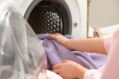 Photo of Woman taking towels out of washing machine in laundry room