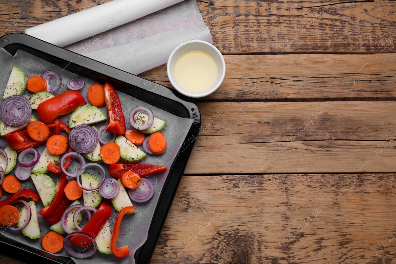 Photo of Baking pan with parchment paper and raw vegetables on wooden table, flat lay. Space for text