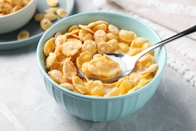Photo of Spoon in bowl with tasty cornflakes and milk on light grey table