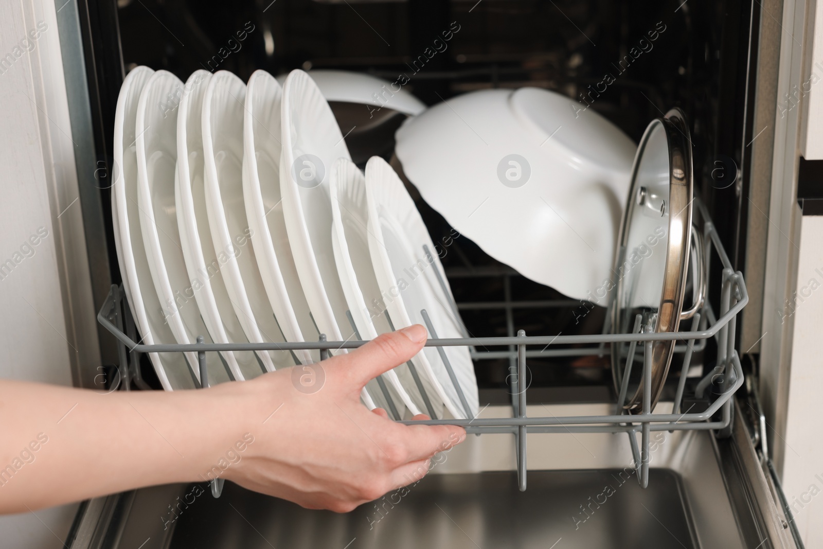 Photo of Woman loading dishwasher with plates indoors, closeup