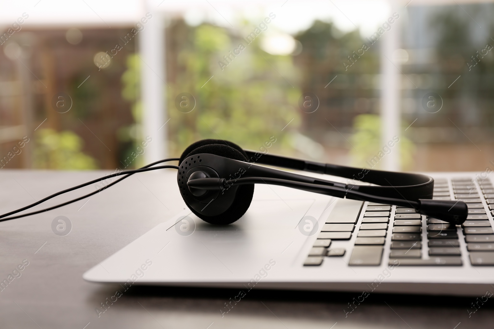 Photo of Modern laptop and headset on table indoors. Technical support concept