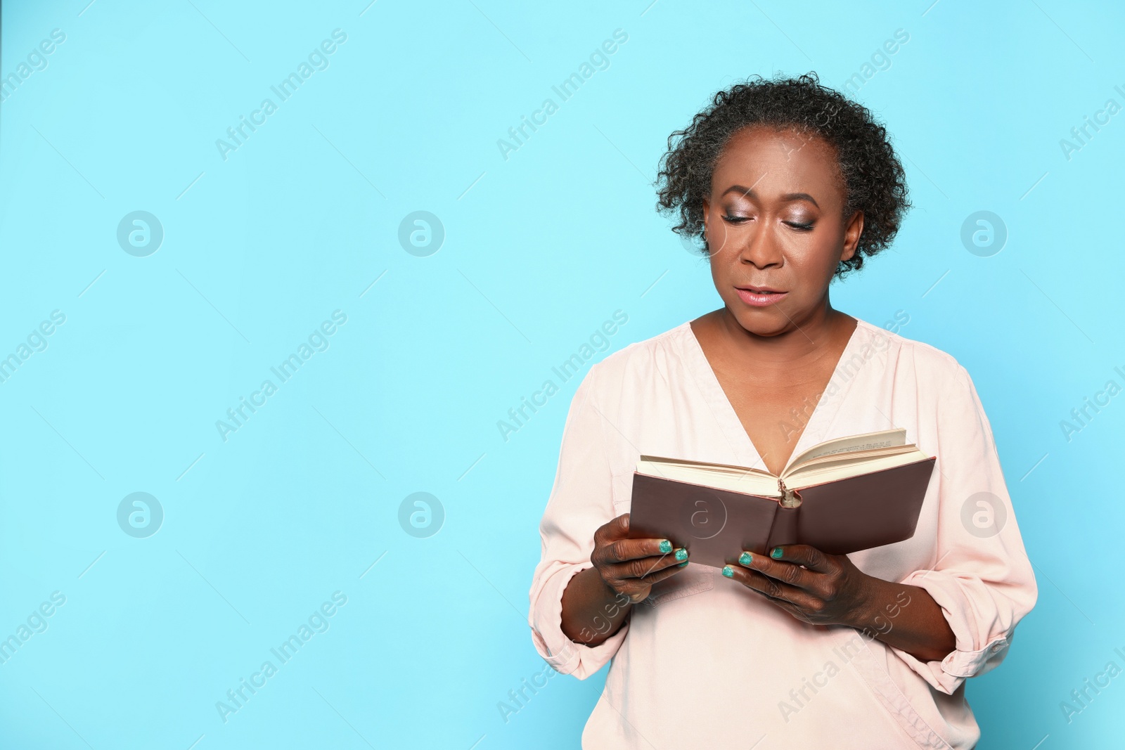 Photo of Portrait of mature African-American woman reading book on light blue background, space for text
