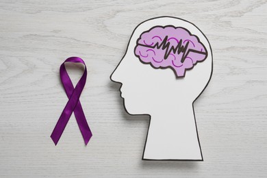 Human head cutout with brain, pulse line and purple ribbon on white wooden background, flat lay. Epilepsy awareness