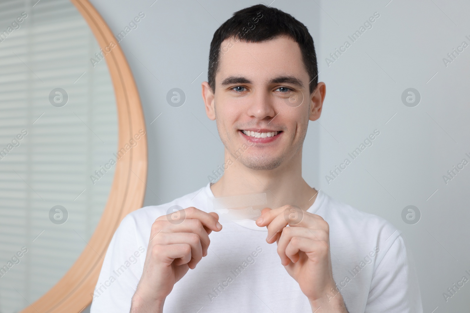 Photo of Young smiling man with whitening strips indoors