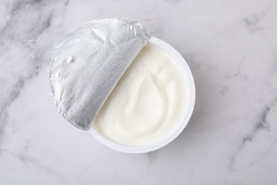 Photo of Delicious natural yogurt in plastic cup on white marble table, top view