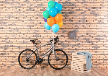 Photo of Bicycle with colorful balloons near brick wall indoors