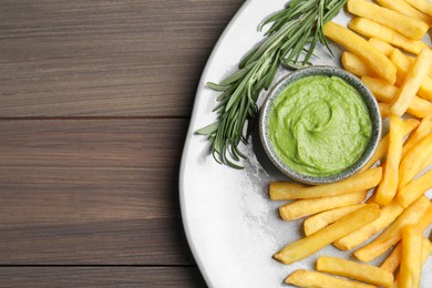 Photo of Plate with delicious french fries, avocado dip and rosemary served on wooden table, top view. Space for text
