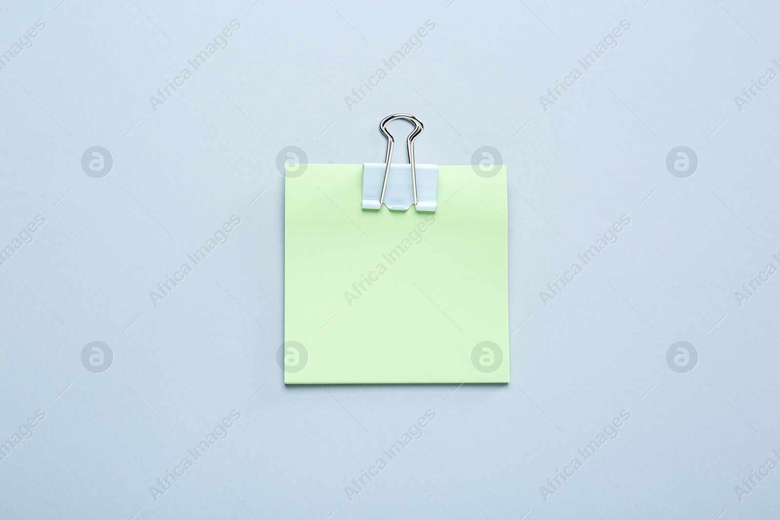 Photo of Blank light green note with white paper clamp on grey background, top view. Space for text