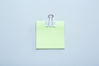 Blank light green note with white paper clamp on grey background, top view. Space for text