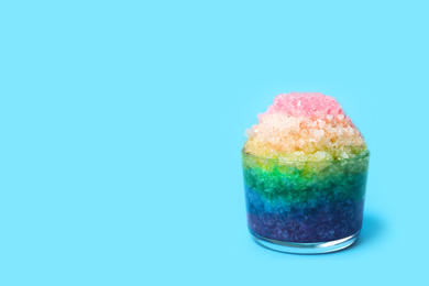 Photo of Rainbow shaving ice in glass dessert bowl on light blue background, space for text