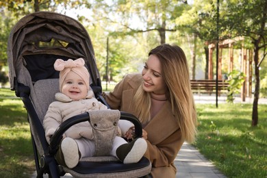 Happy mother with her little baby in stroller at park on sunny day