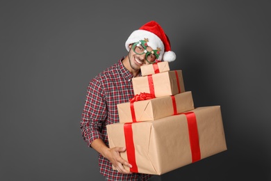 Young man with Christmas gifts on grey background