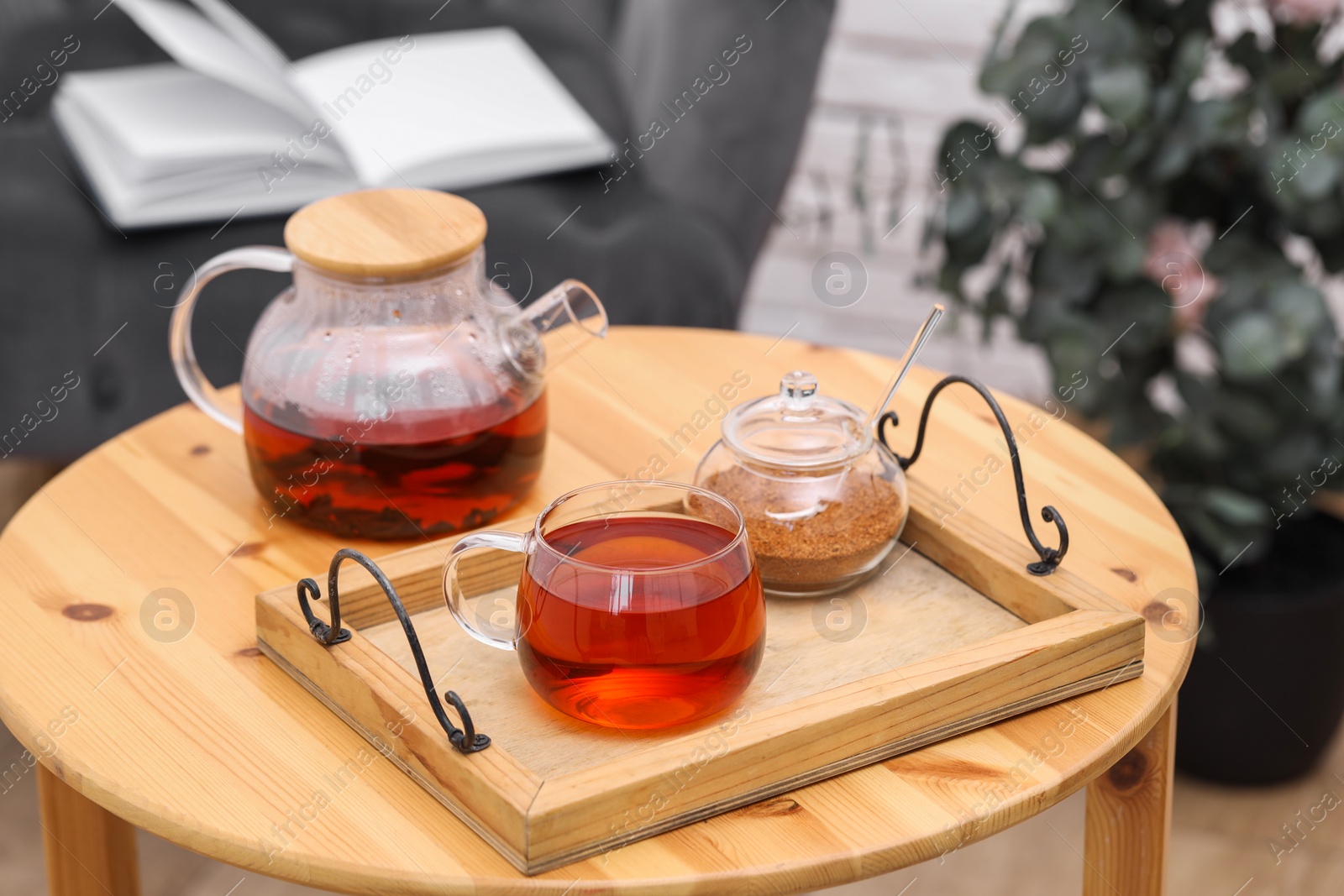 Photo of Teapot, cup of aromatic tea and brown sugar on wooden table indoors
