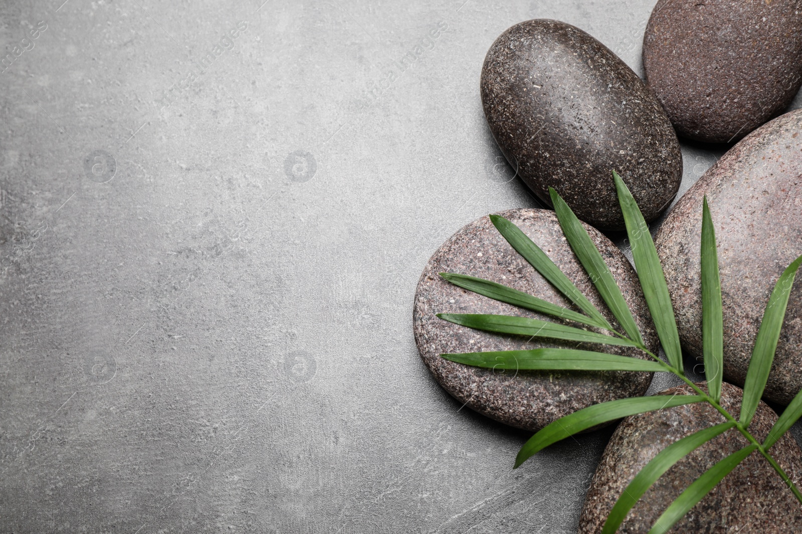 Photo of Spa stones and palm leaf on grey table, flat lay. Space for text