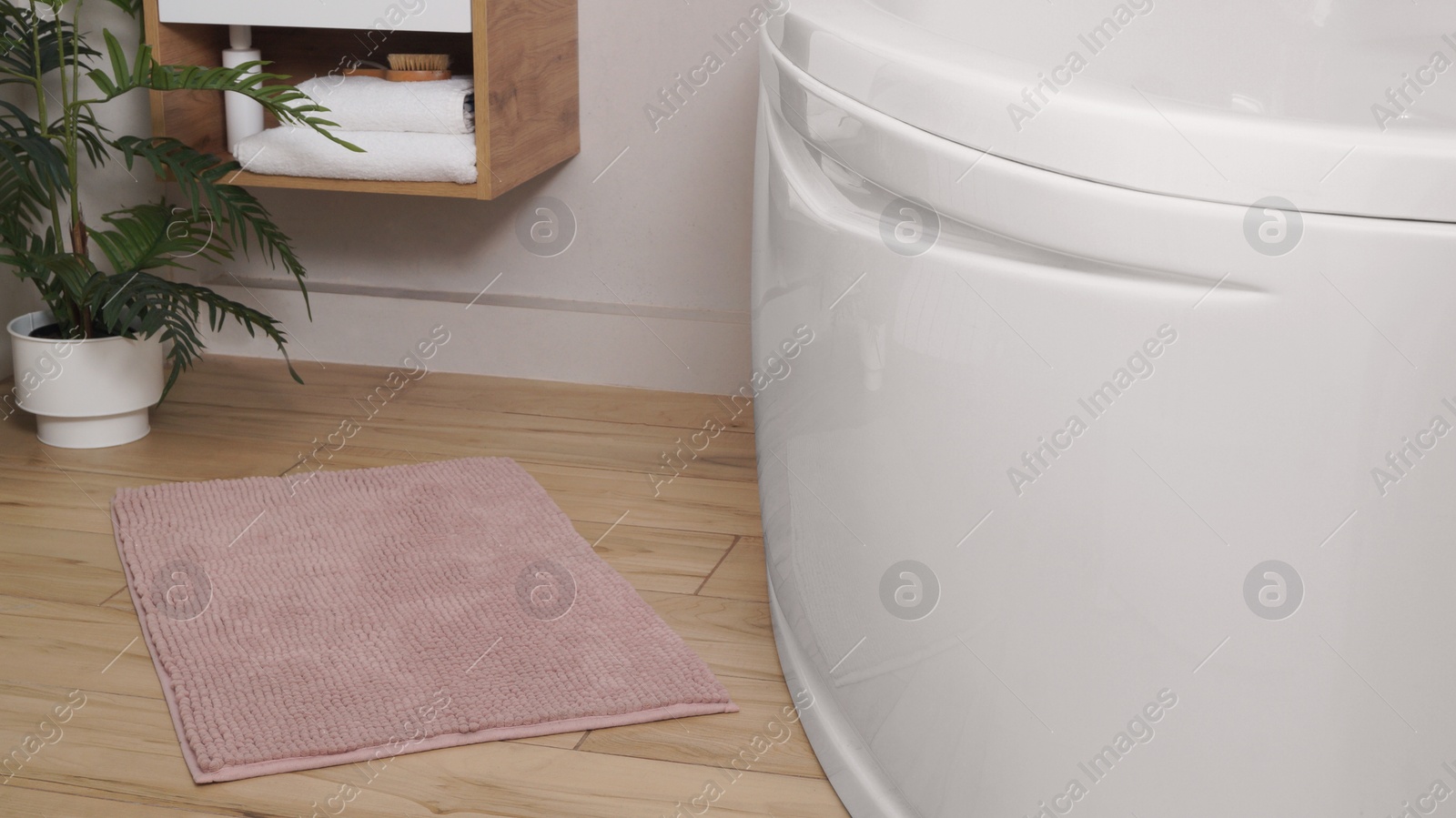 Photo of Soft bath mat near tub on wooden floor in bathroom