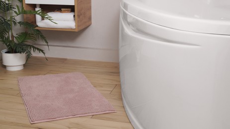 Soft bath mat near tub on wooden floor in bathroom