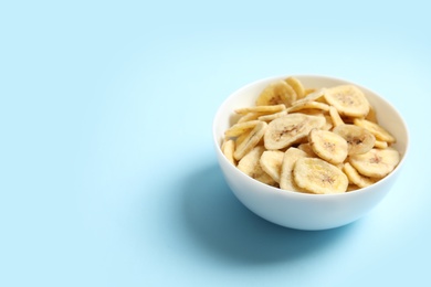 Bowl with banana slices on color background, space for text. Dried fruit as healthy snack