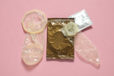 Unrolled female, male condoms and packages on light pink background, flat lay. Safe sex