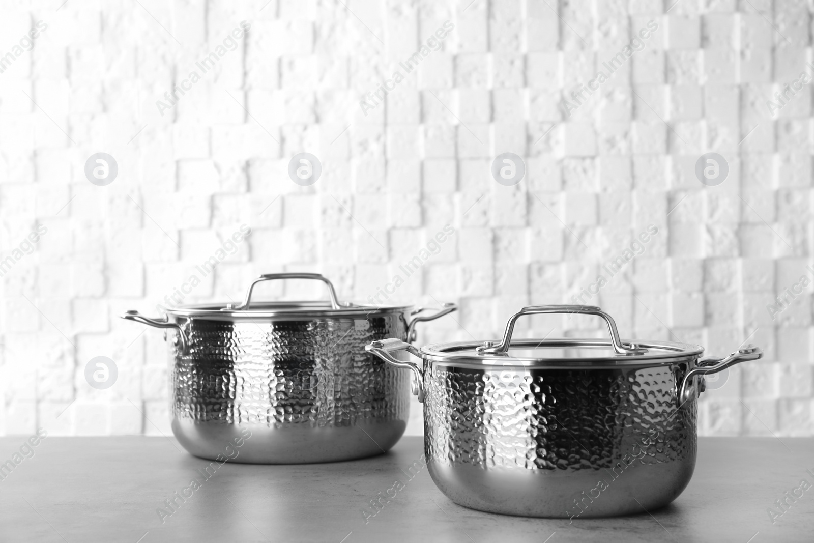 Photo of New clean saucepans on table against white wall, space for text