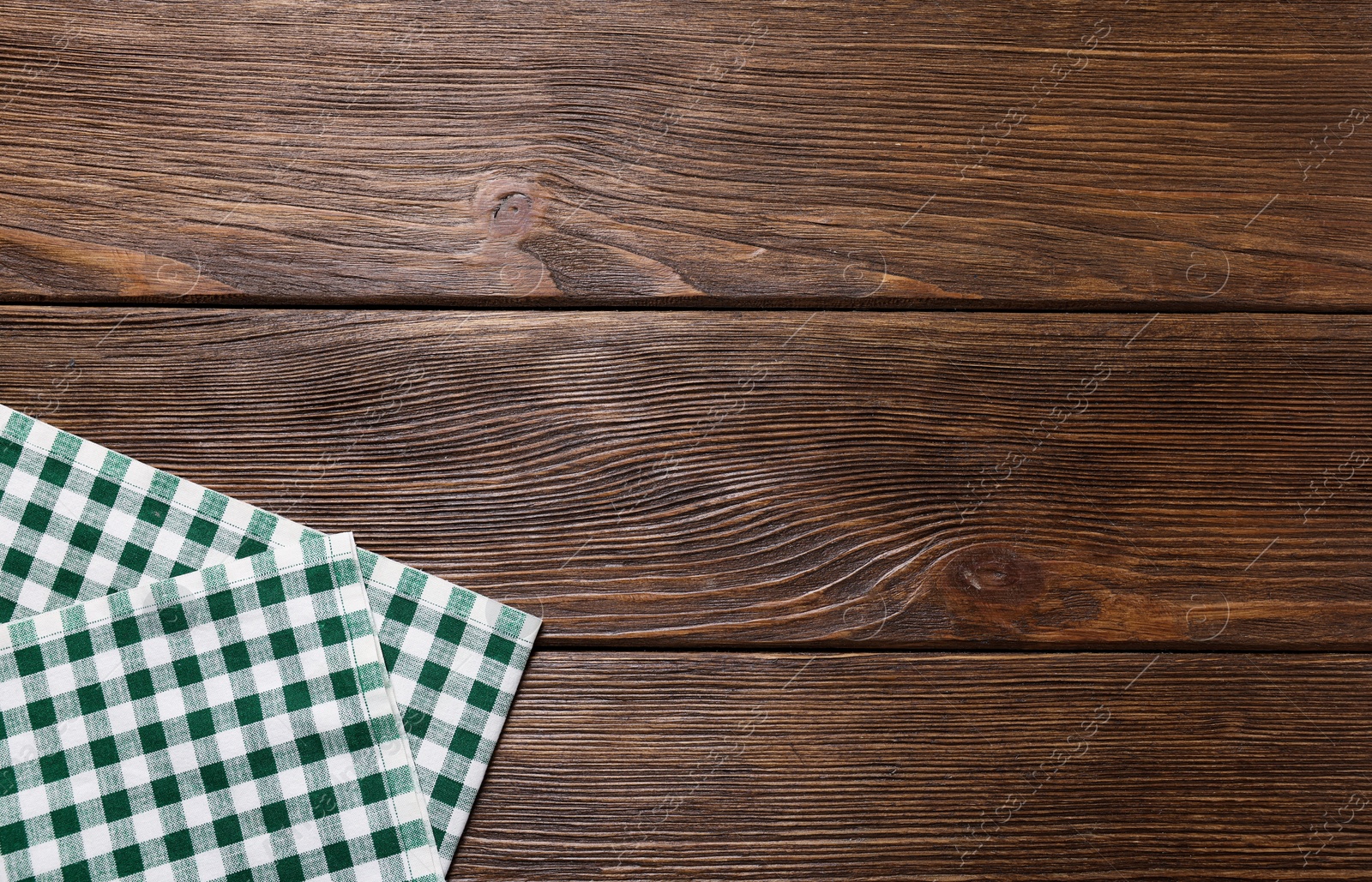 Photo of Green checkered tablecloth on wooden table, top view. Space for text