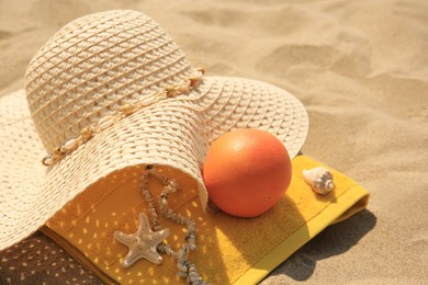 Photo of Straw hat, towel and orange on sand, closeup