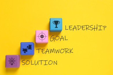 Image of Colorful cubes with different images and words Leadership, Goal, Teamwork and Solution on yellow background, flat lay