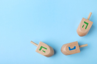 Photo of Hanukkah traditional dreidels with letters He and Nun on light blue background, flat lay. Space for text