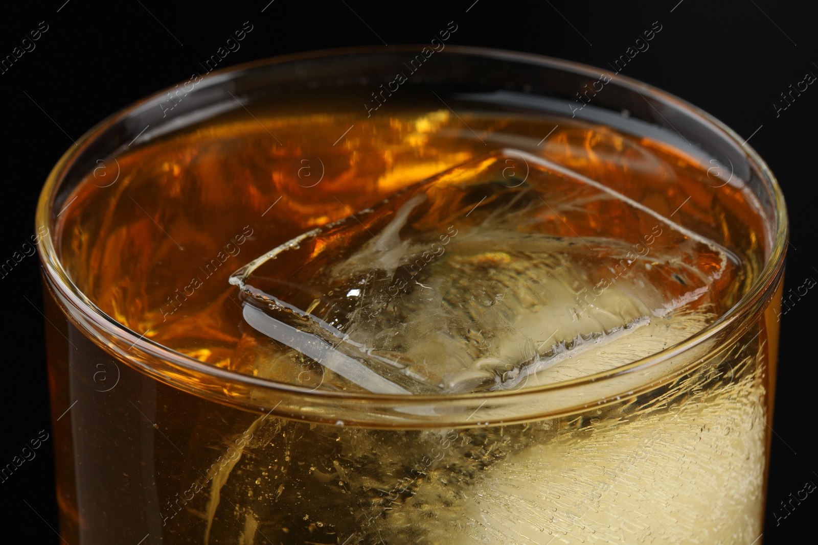 Photo of Tasty whiskey and ice in glass on black background, closeup