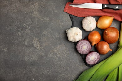 Photo of Fresh whole and cut onions, leek, garlic on grey table, flat lay. Space for text