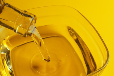 Pouring cooking oil from bottle into bowl on yellow background, closeup
