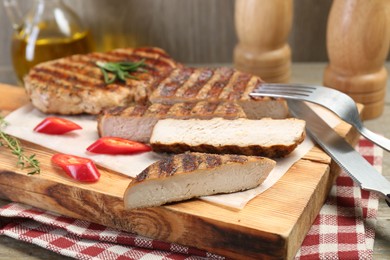 Photo of Cut grilled pork steaks and cutlery on table, closeup