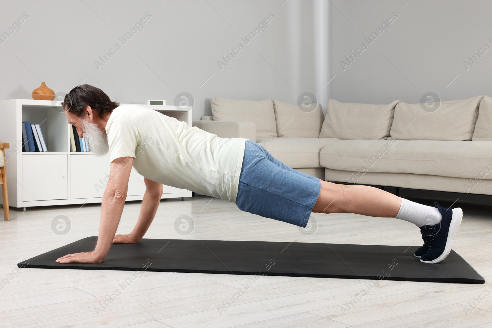 Photo of Senior man in sportswear doing exercises on fitness mat at home