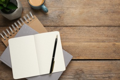 Photo of Notebooks, pen, cup of coffee and plant on wooden table, flat lay. Space for text