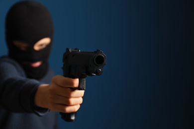 Photo of Man in mask holding gun against dark blue background, focus on hand. Space for text