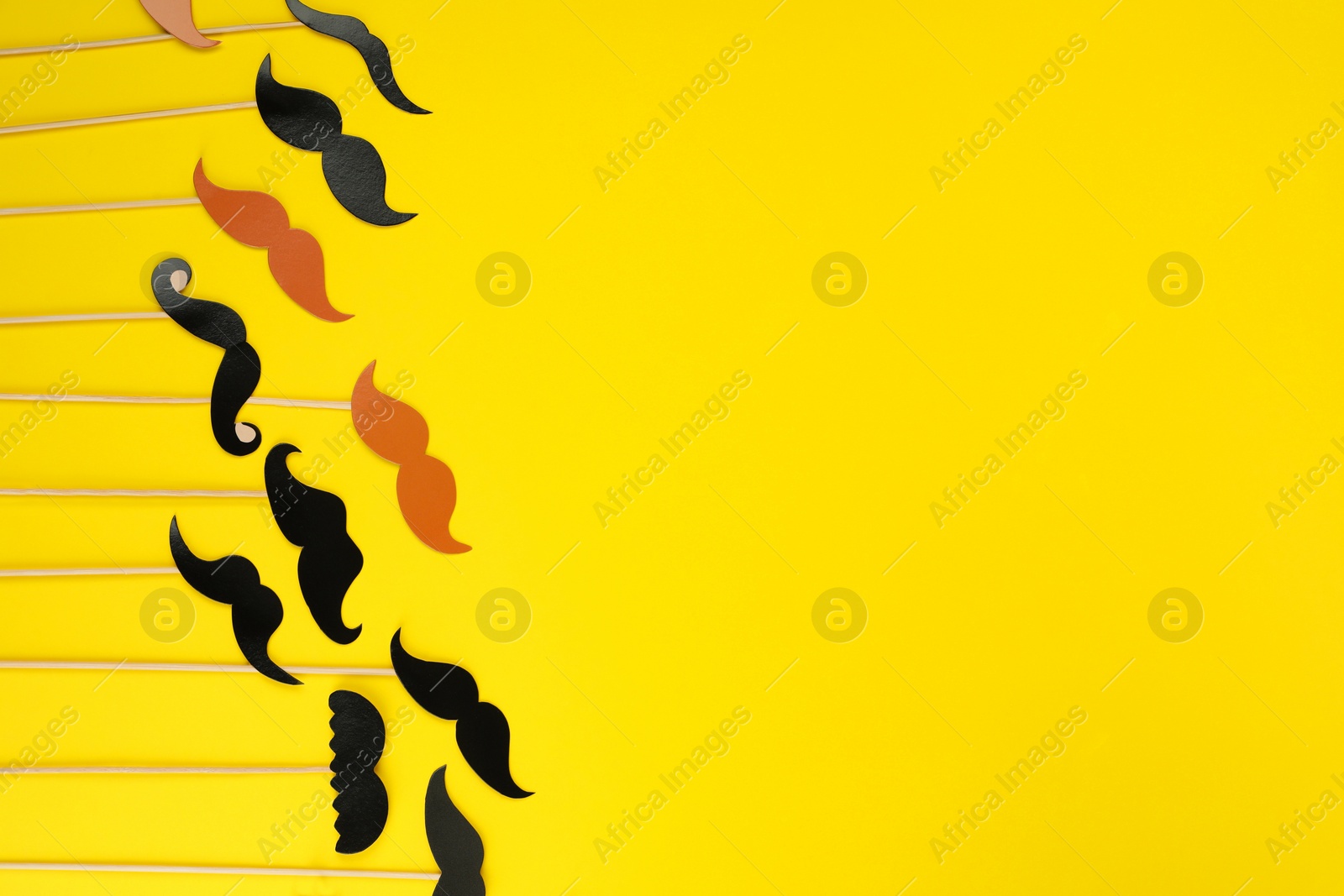 Photo of Fake paper mustaches with sticks on yellow background, flat lay. Space for text