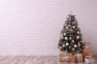 Beautifully decorated Christmas tree and gift boxes  near white brick wall, space for text