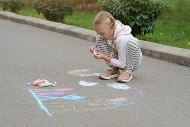Photo of Little child drawing her hands with chalk outdoors