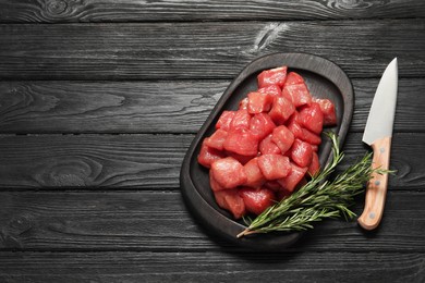 Cooking delicious goulash. Raw beef meat, rosemary and knife on black wooden table, flat lay. Space for text