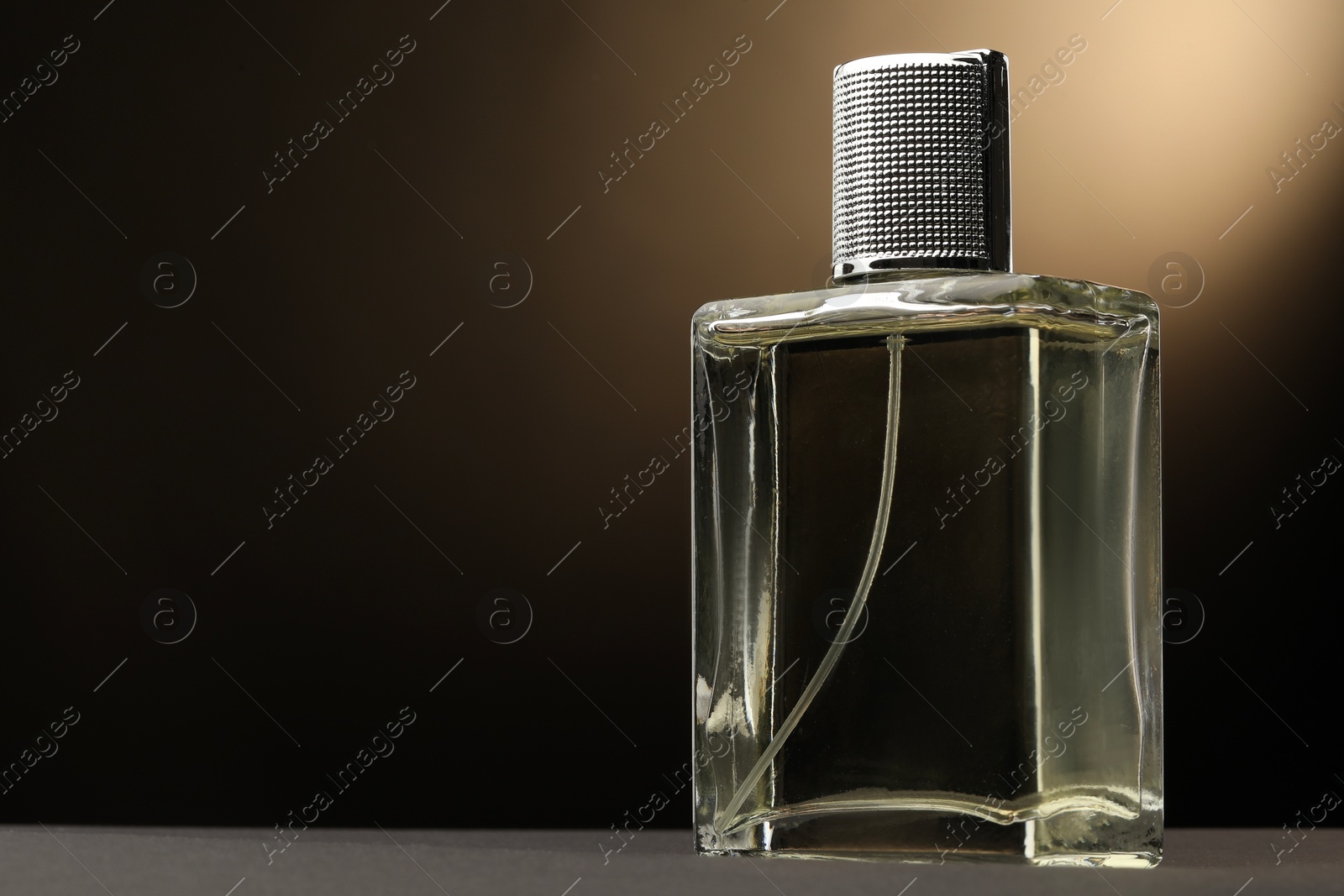 Photo of Luxury men`s perfume in bottle on grey table against brown background, space for text