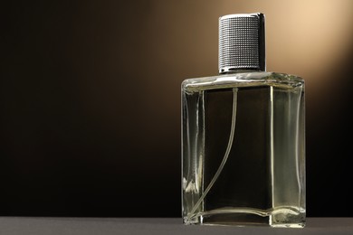 Photo of Luxury men`s perfume in bottle on grey table against brown background, space for text
