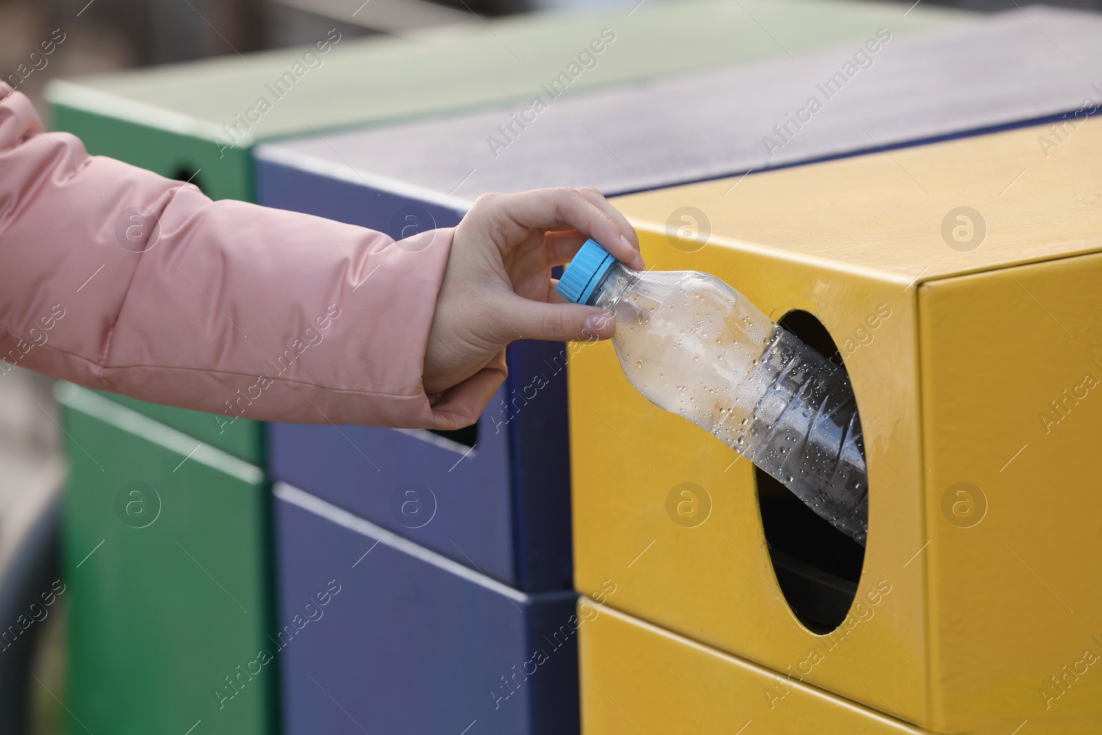 Photo of Woman throwing plastic bottle into garbage bin outdoors, closeup. Waste sorting