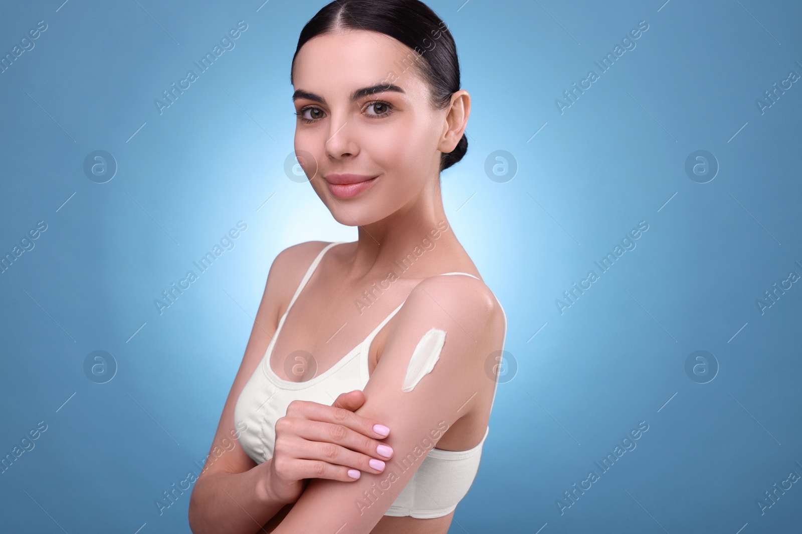 Photo of Beautiful woman with smear of body cream on her shoulder against light blue background. Space for text