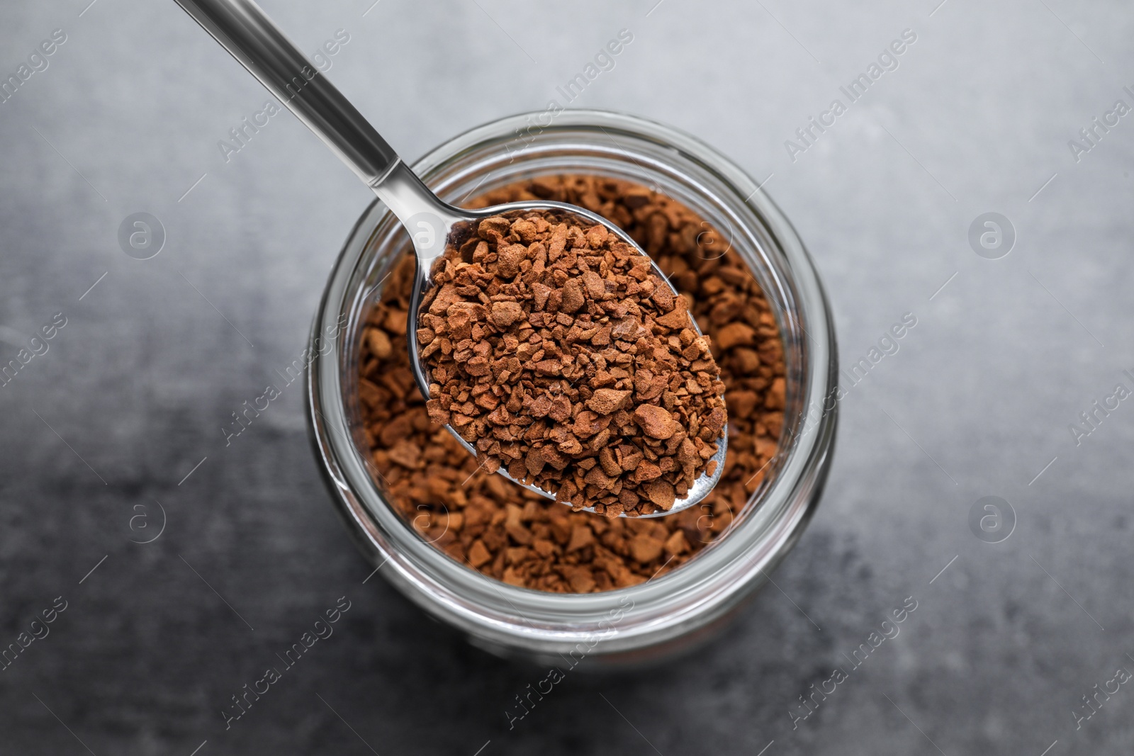 Photo of Instant coffee and spoon above glass jar on grey table, top view