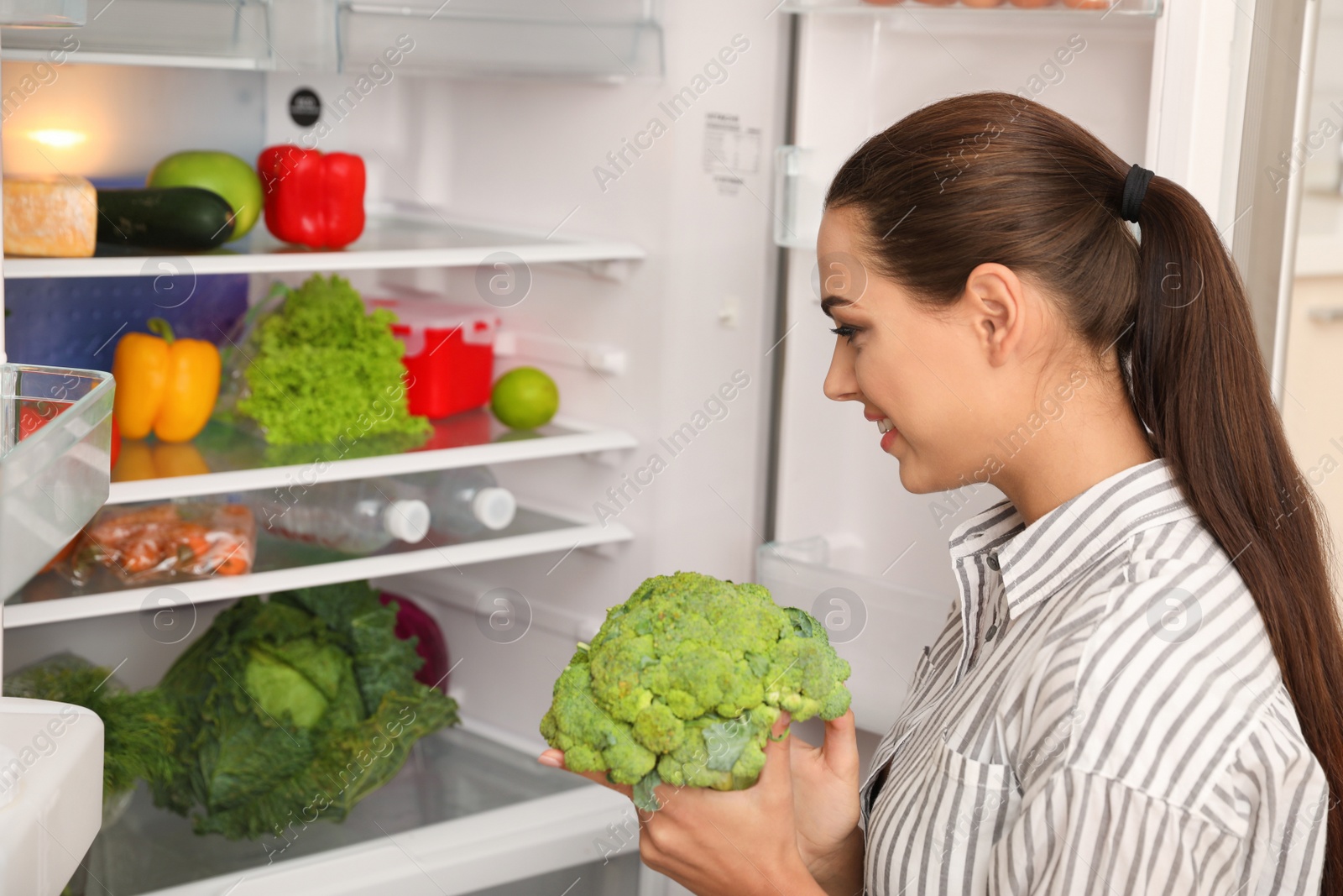 Photo of Young woman choosing products from refrigerator in kitchen