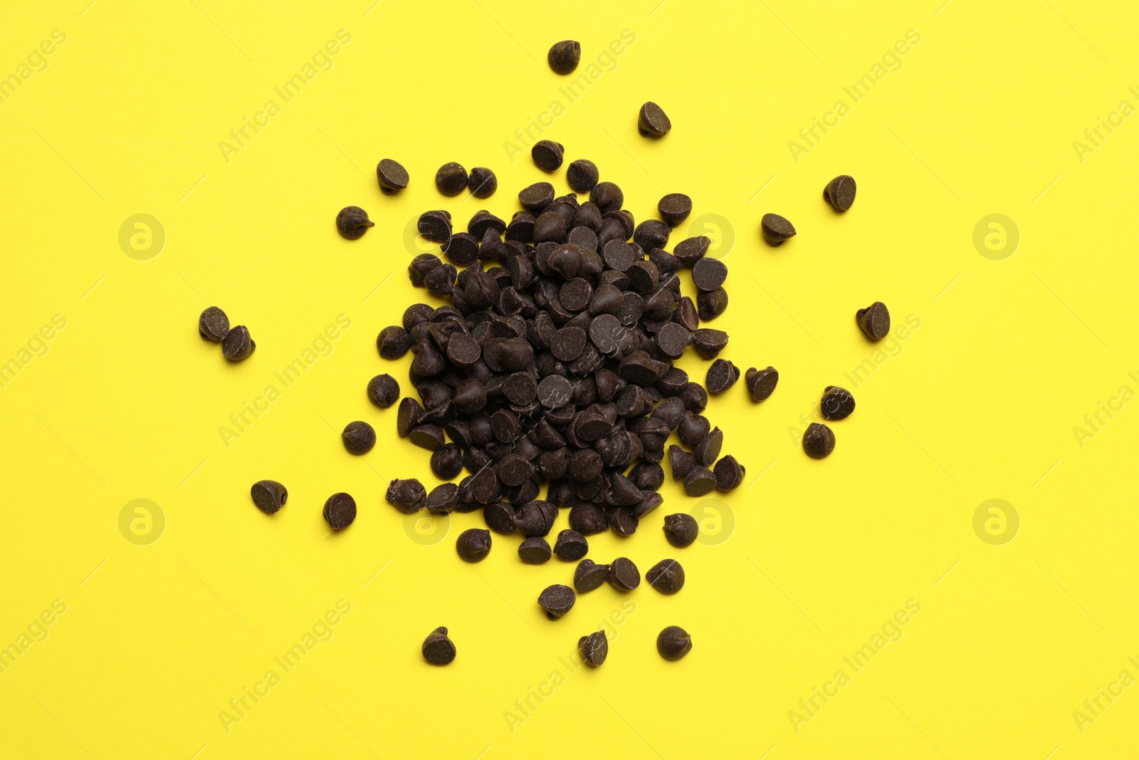 Photo of Pile of delicious chocolate chips on yellow background, top view