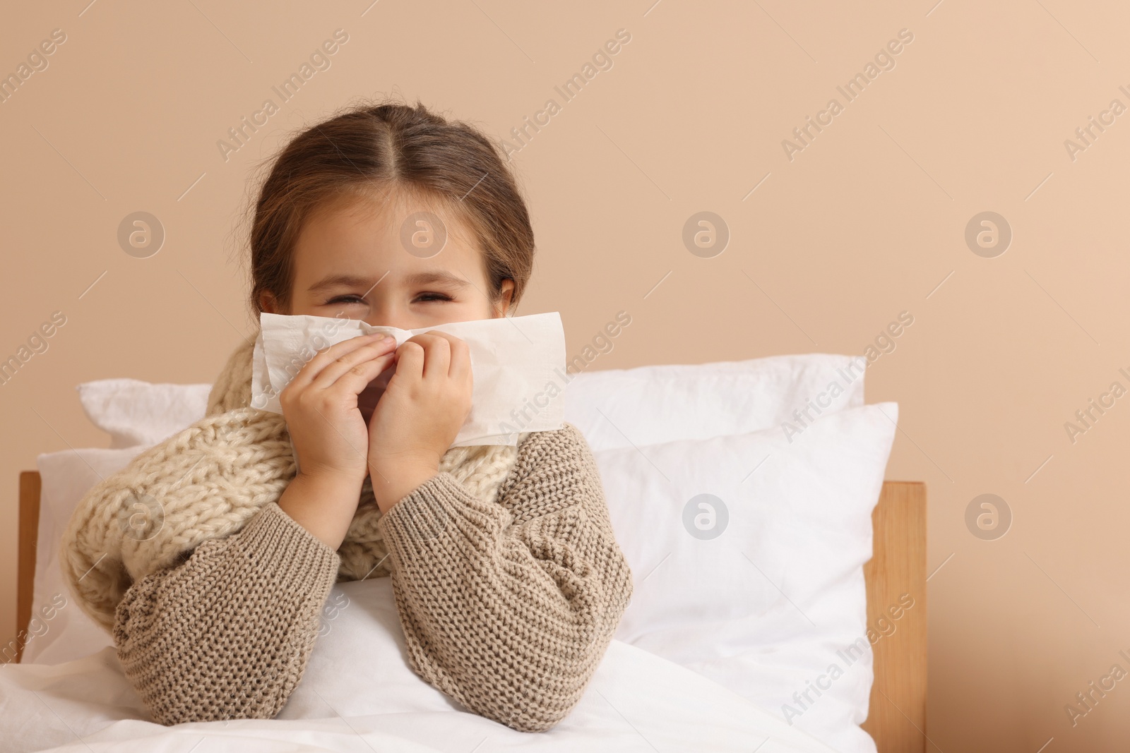 Photo of Girl blowing nose in tissue on bed in room. Cold symptoms