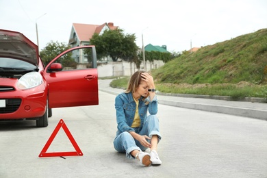 Photo of Upset woman sitting near warning triangle and broken car on road