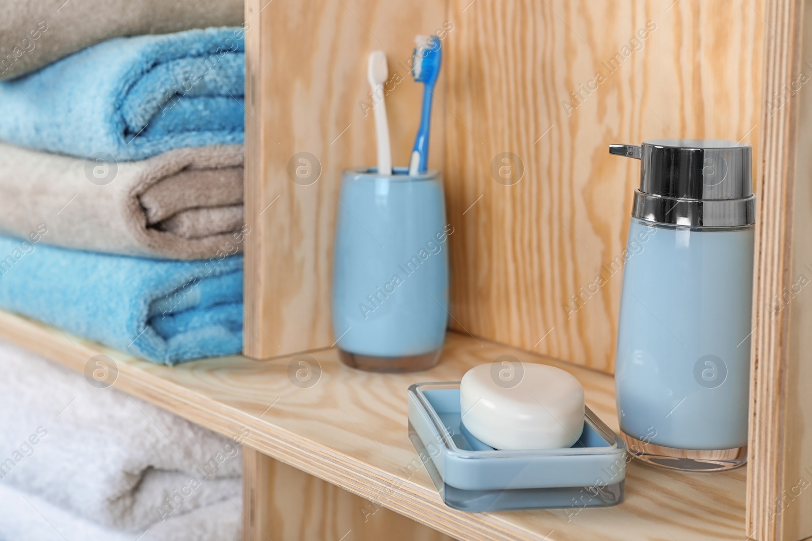 Photo of Dish with soap, bottle of shampoo and toothbrushes on wooden shelf