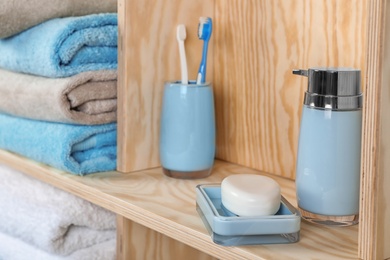 Photo of Dish with soap, bottle of shampoo and toothbrushes on wooden shelf